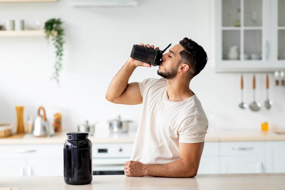 man drinking protein shake in kitchen