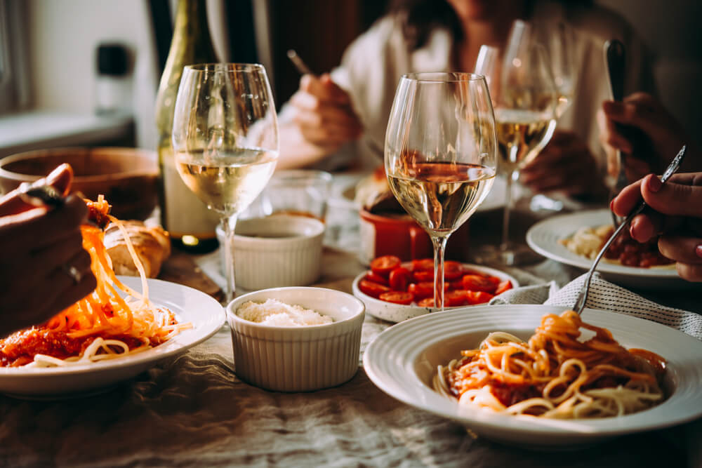 People eating vegetarian pasta at a dinner table with white wine